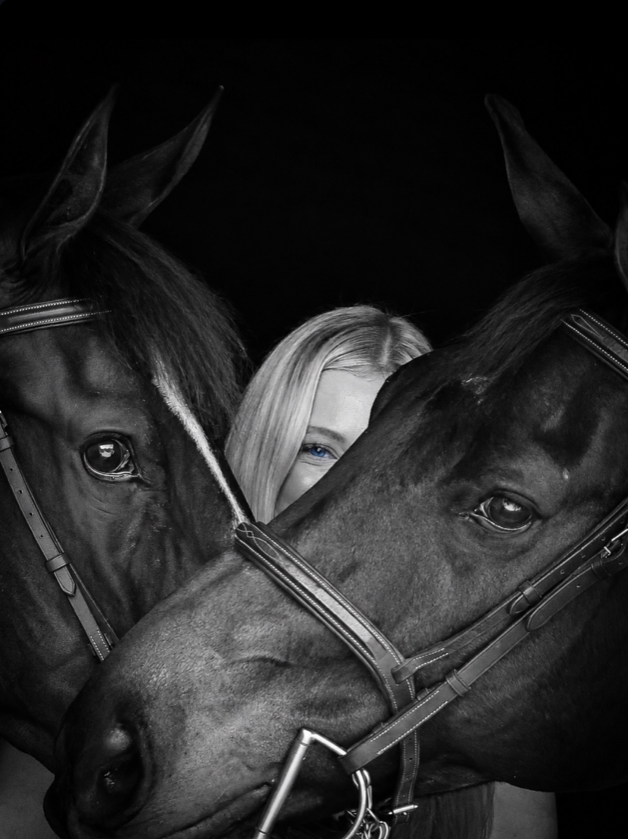 Two dark horses framing a woman in a mostly black-and-white portrait