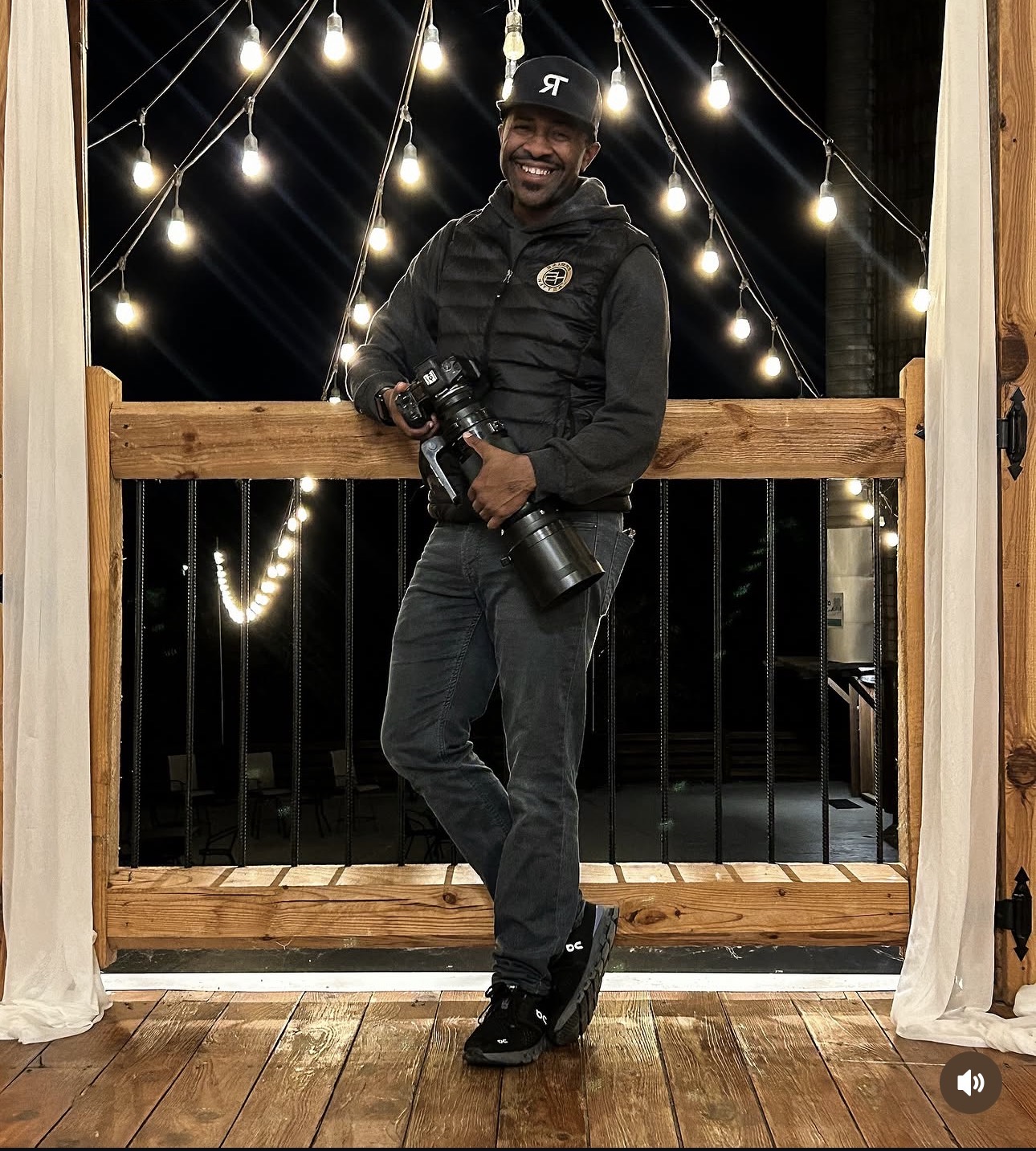 Steven Pelzer smiling and holding his camera beneath string lights